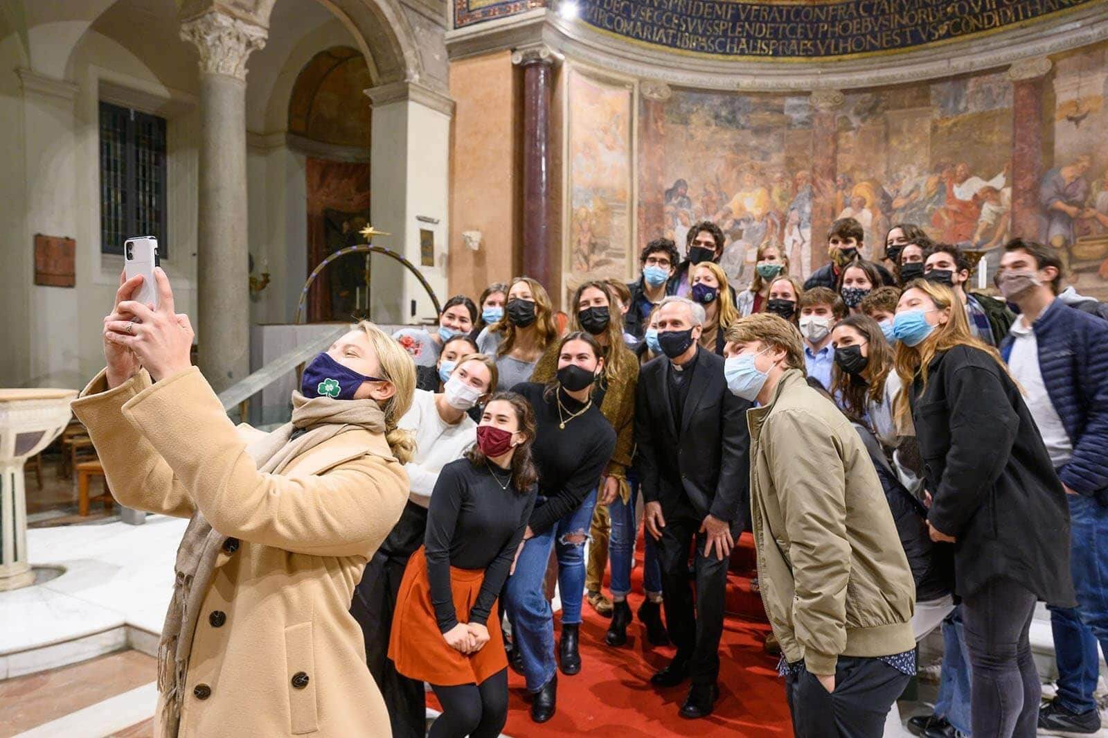 One masked student with a camera takes a group selfie with Fr. Jenkins and several other Notre Dame students.