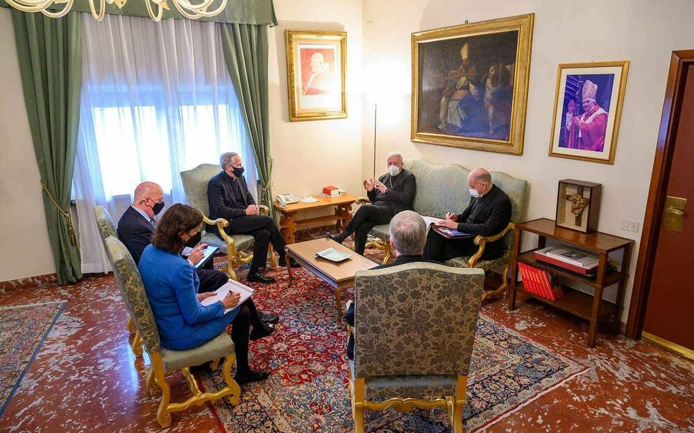 Six people meet in the Cardinal’s Vatican office.