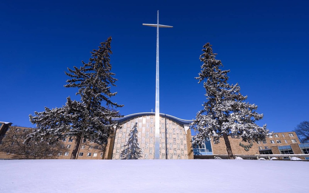 Moreau Seminary chapel and stainless steel cross between two trees during a clear day in January.