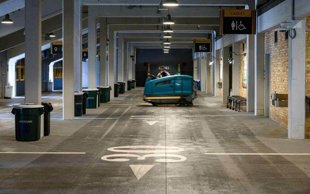 A man uses a floor cleaning machine in a stadium concourse.