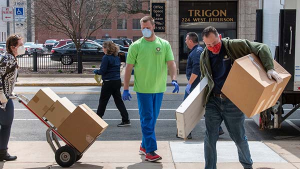Three people wearing masks unload boxes.