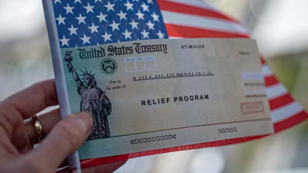 A US Treasuring relief program check held in front of an American flag.
