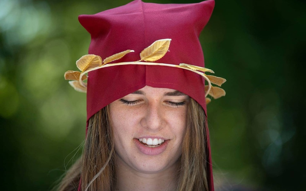 A student wearing a red cap and faux gold leaves.