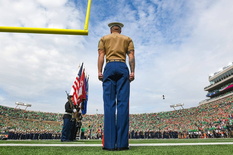 ROTC member at attention stance stands at the end zone of the stadium.