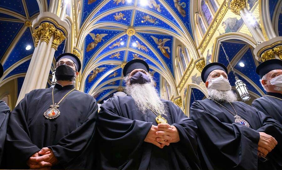 Three masked clergy members stand inside of the Basilica.