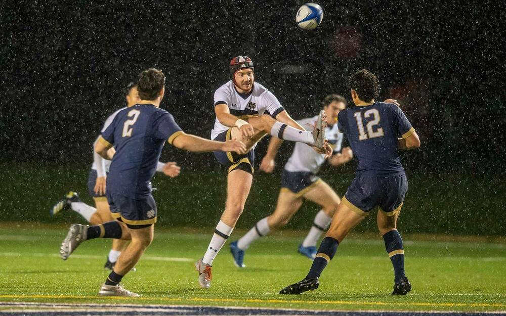 Rugby players jump for the ball as it rains.