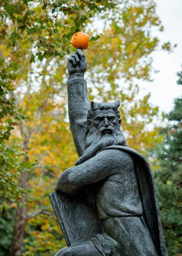 Moses statue outside with a pumpkin on its finger.