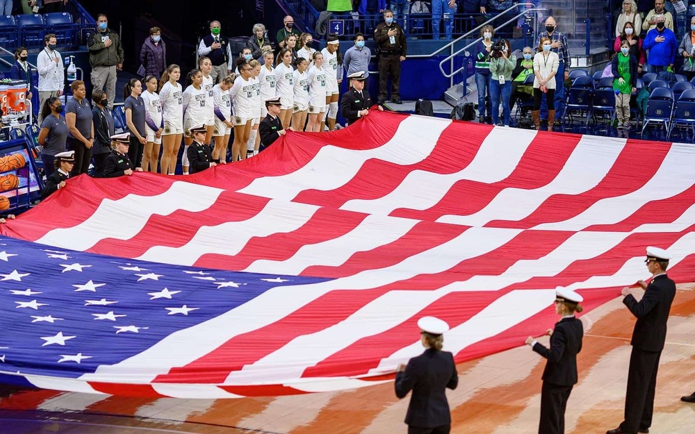 Navy ROTC midshipmen hold an oversize U.S. Flag before a Women’s Basketball game.