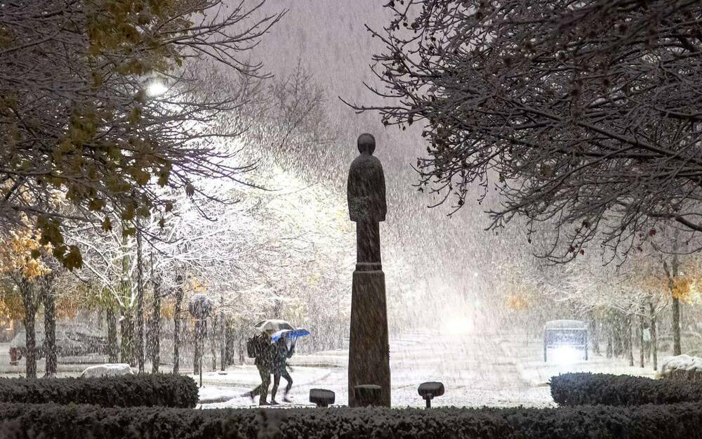 Two people walk on campus at desk while it snows.