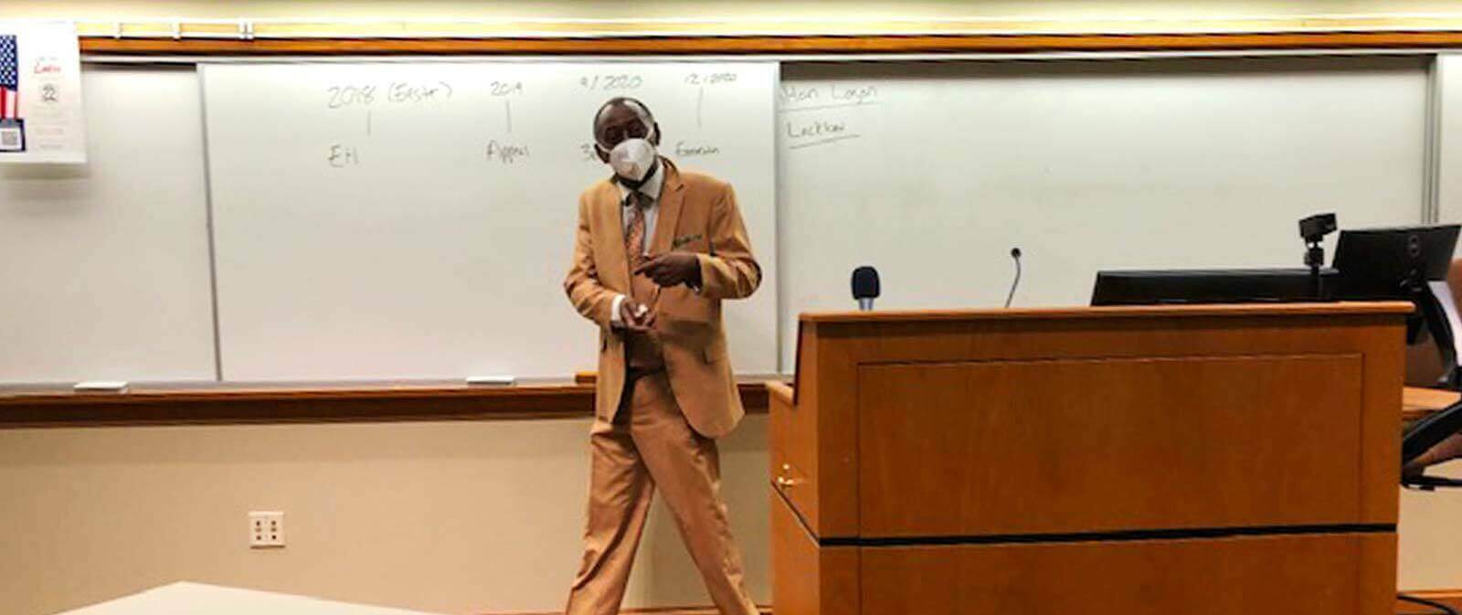 A man wearing a mask in front of a classroom.