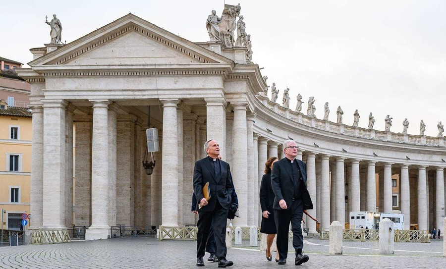 A group of four people, including two priests, walk outside.