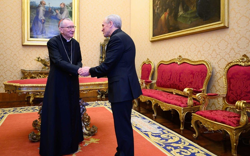 A priest and cardinal priest shake hands and talk.