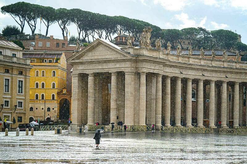A rain shower at St. Peter's Square. People walk around the Square with umbrellas.