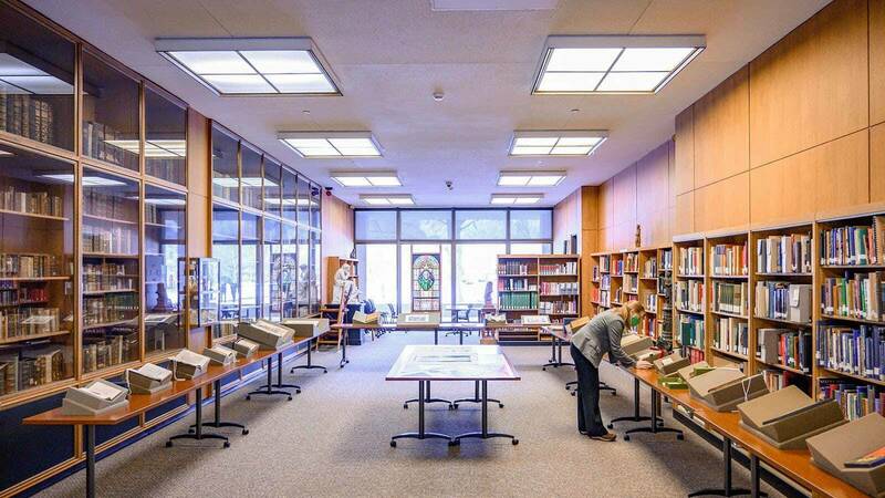 Book shelves and glass containers on each side of a room. A woman leans over to look at a book on a table.