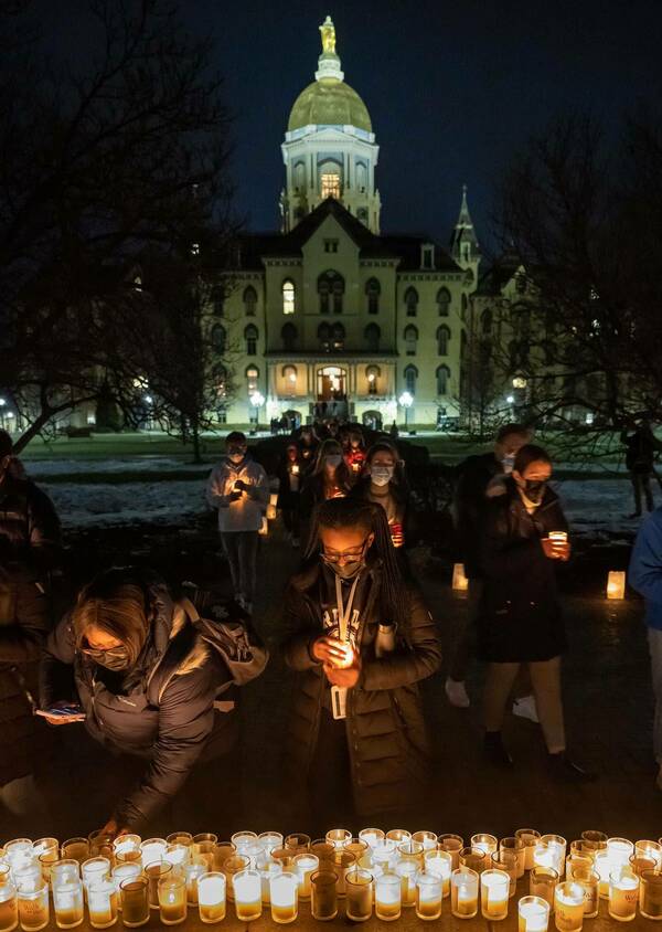A line of people outside of Notre Dame's Main Building hold candles and set them down on a concrete wall.