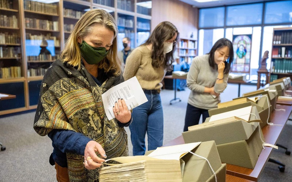 Three masked people look at books propped up on a table.