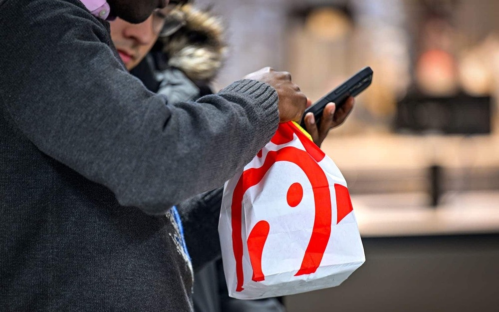 An individual texts on a phone while holding a Chick-fil-A bag.
