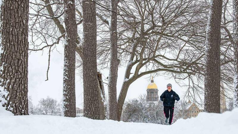 A student jogs on a snowy trail. The Main Building is off in the distance.