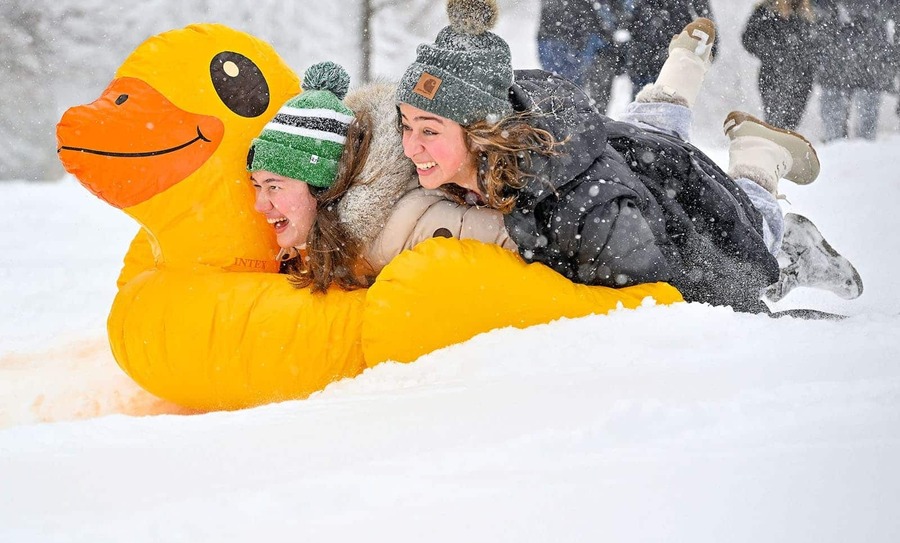 Two students on top of a inflatable duck sled down a small hill.
