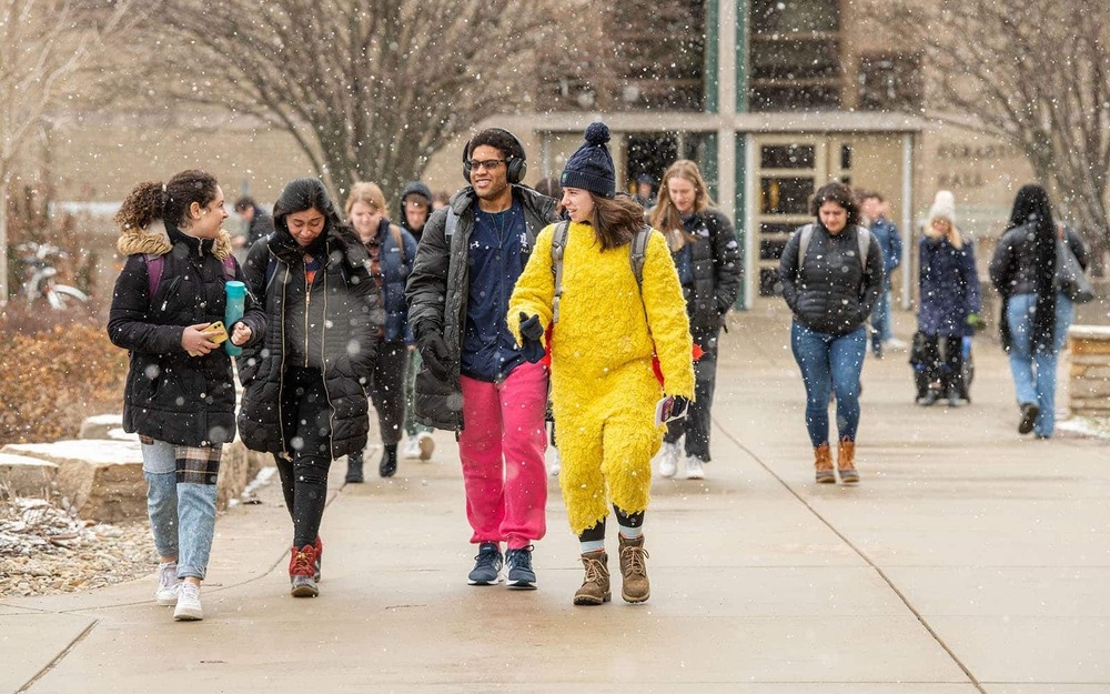 Students walk and talk to class during a snow flurry. One student wears part of a yellow bird suit.