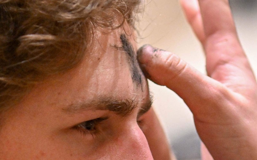 A close up shot of someone putting an ash cross on another's forehead.