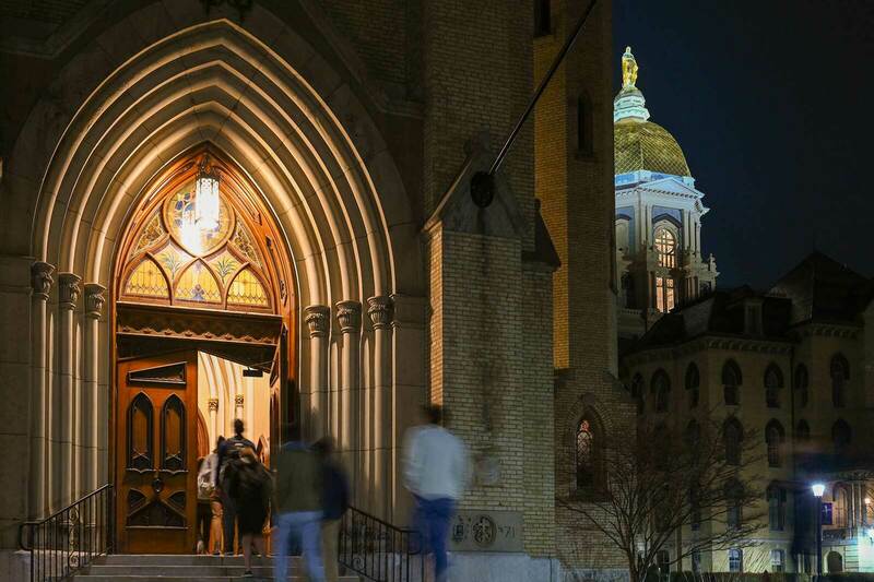 Students enter the Basilica of the Sacred Heart. The Golden dome illuminates against the dark sky.