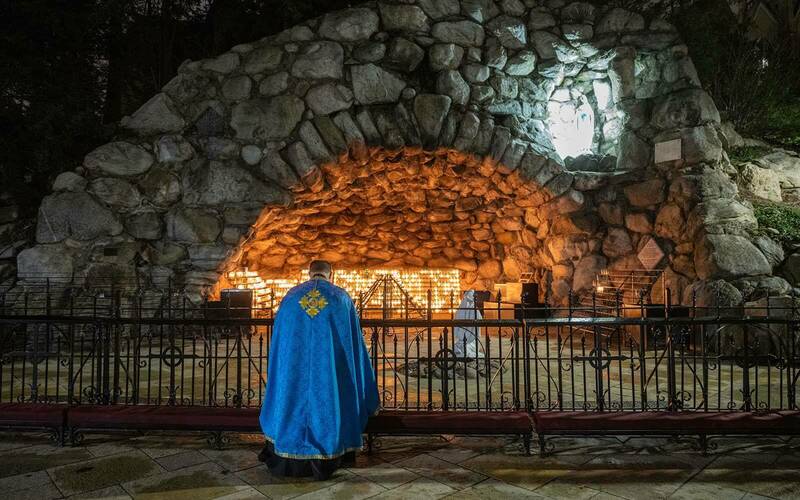 A priest kneels at the grotto.