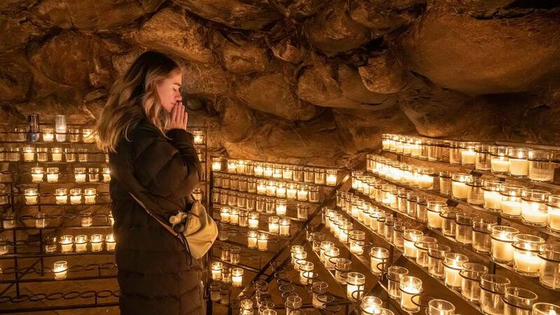 A woman prays inside of the Grotto in front of a row of candles.