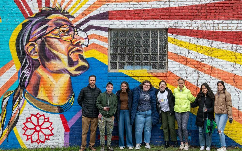 A group poses for a photo in front of a paint mural on the side of a building.