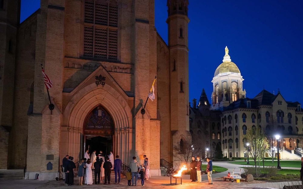 A group of people stand outside the Basilica at night. Behind the Golden Dome glows.