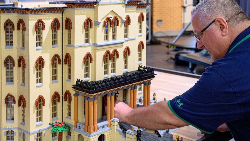 A man places a LEGO on a LEGO building that represents the Main Building.