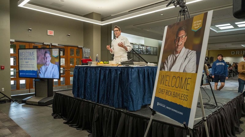 Chef Rick Bayless stands at a table on a small stage.