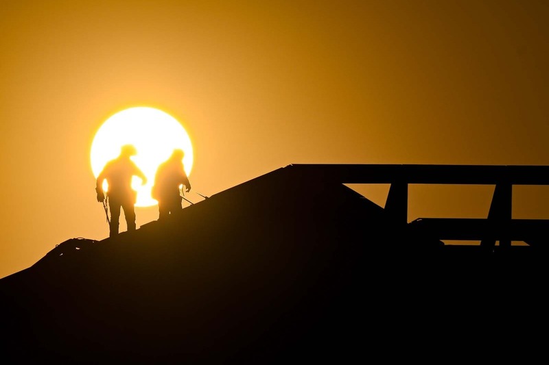 Two construction workers' stand on a building. Their silhouettes in front of the morning sun.