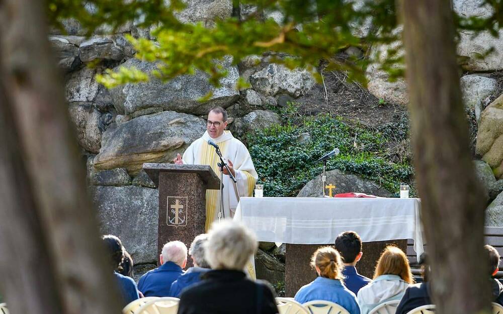 A priest speaks to people in front of the Grotto.