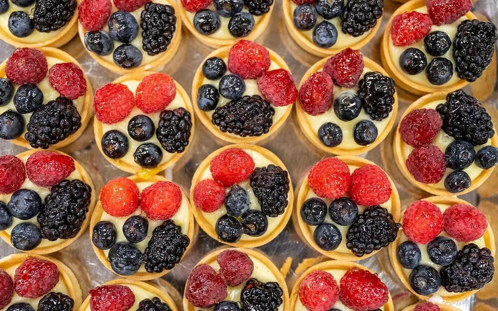 Fruit tarts with blueberries, raspberries, and black raspberries organized neatly on a sheet pan.