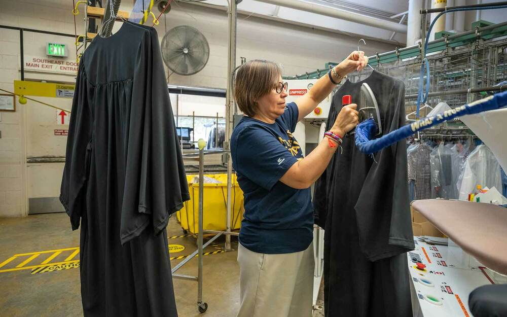 A woman steam presses a black graduation robe.