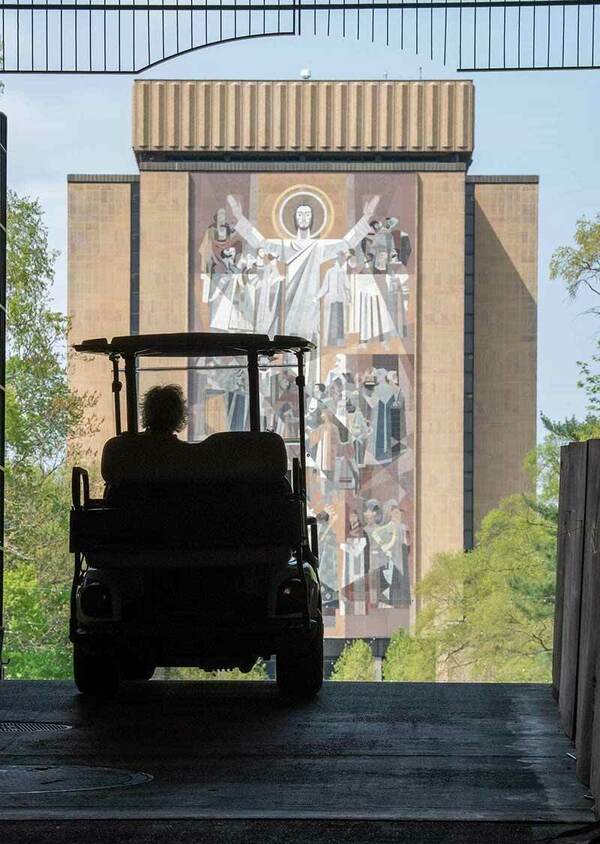 A silhouette of an individual driving a golf cart towards The Word of Life Mural, also known as Touch Down Jesus.