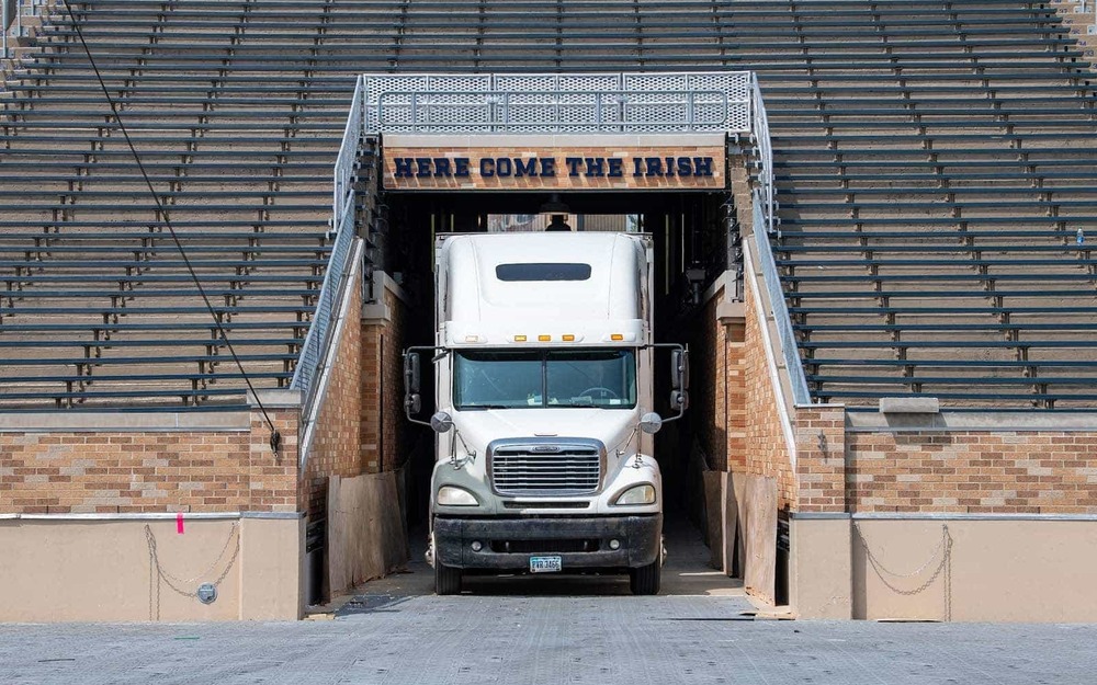 A semi truck enters through the tunnel of the Notre Dame Stadium. Above the tunnel says 