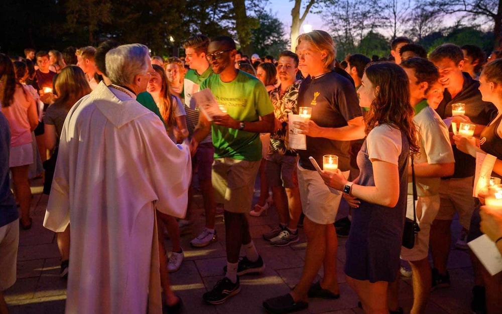 Fr. John Jenkins, C.S.C. greets graduating seniors, all holding candles, at the Grotto.
