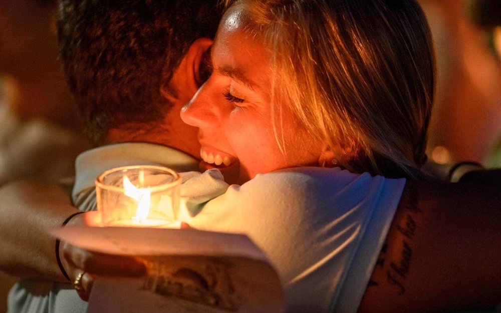 Two people hug each other, one holding a candle.