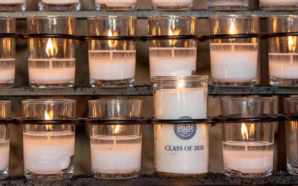 Eight lit candles, one taller than all of the others and has a label that says Class of 2020 and the University of Notre Dame seal.