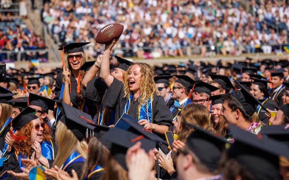 Graduate Edie Uebelhor catches the football thrown by Archbishop Borys Gudziak during his Commencement address.