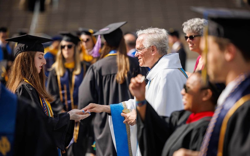 University of Notre Dame president John I Jenkins, C.S.C., hands sacramental bread to a graduate during mass before the Commencement Ceremony.