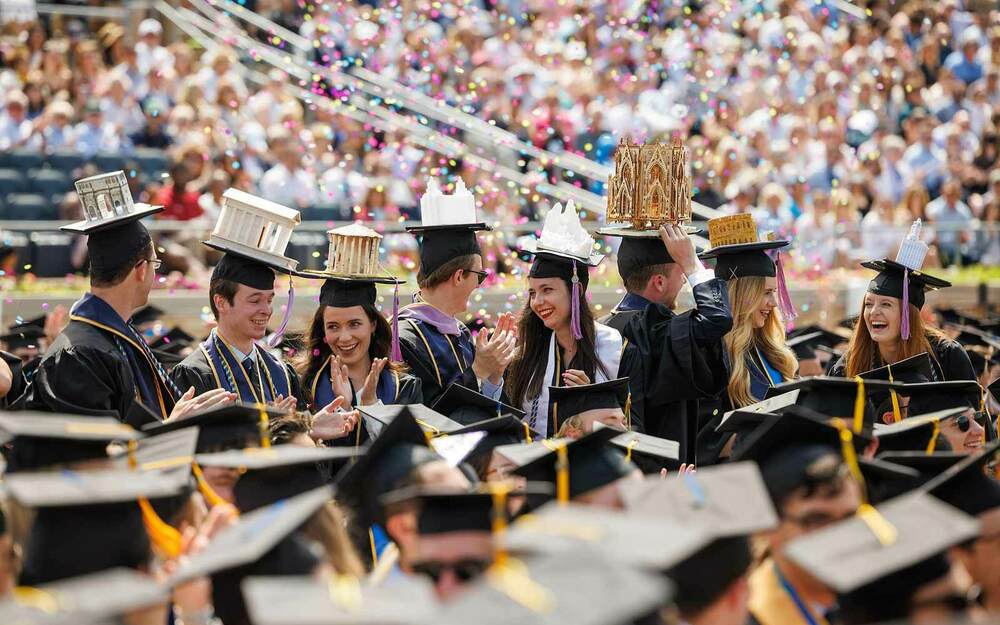 Architecture graduates with decorated caps celebrate during the Commencement Ceremony in Notre Dame Stadium.