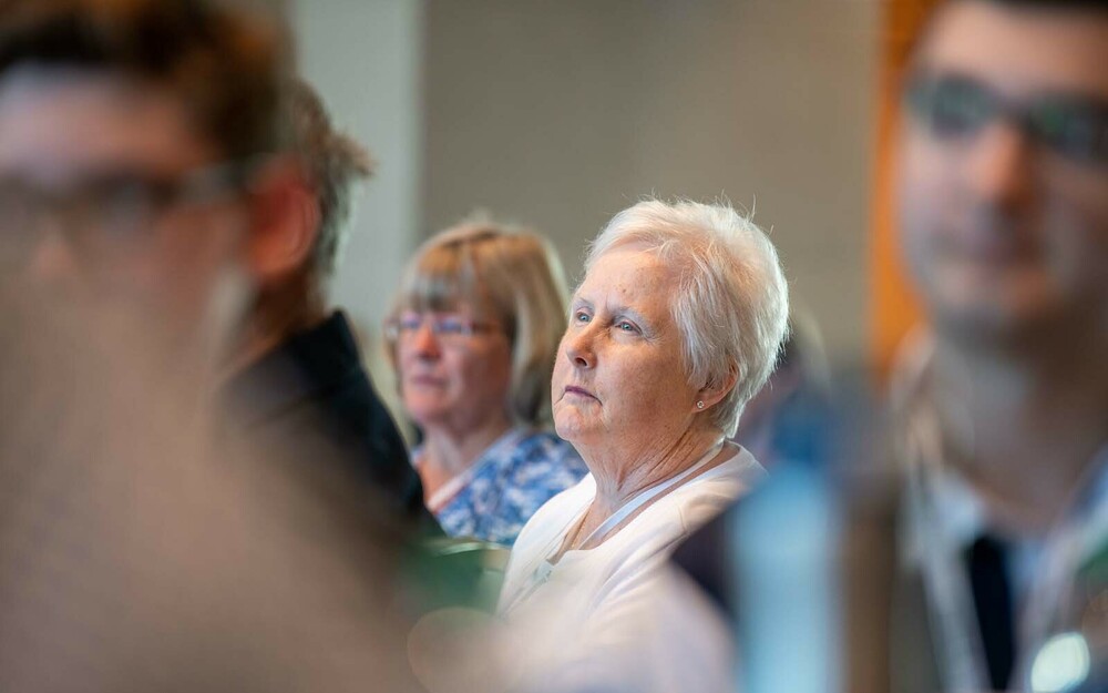 A close up of an older woman with white hair listening to someone speak.