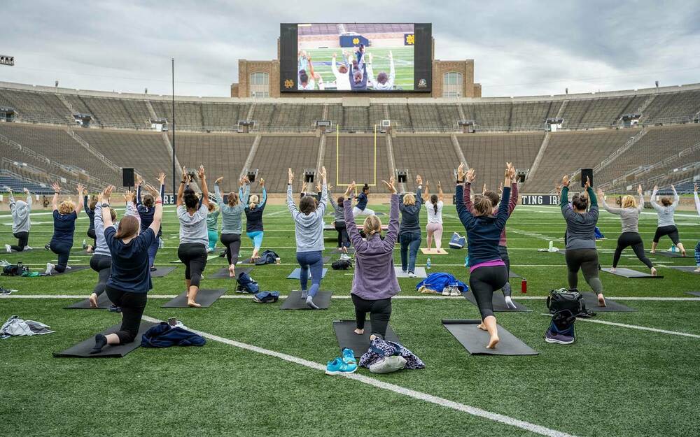 A group of women participate in a yoga class inside of a football stadium.