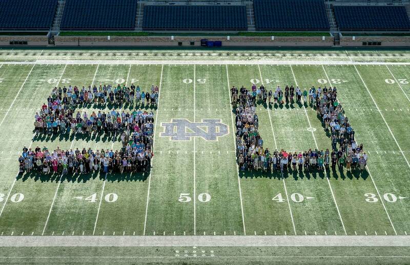 Female graduates of the University of Notre Dame stand in the shape of a 5 and 0 on the field at Notre Dame Stadium.