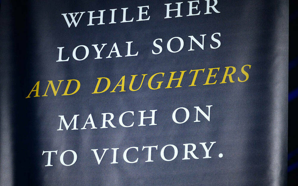 A banner that reads 'While her loyal sons and daughters march on to victory.'