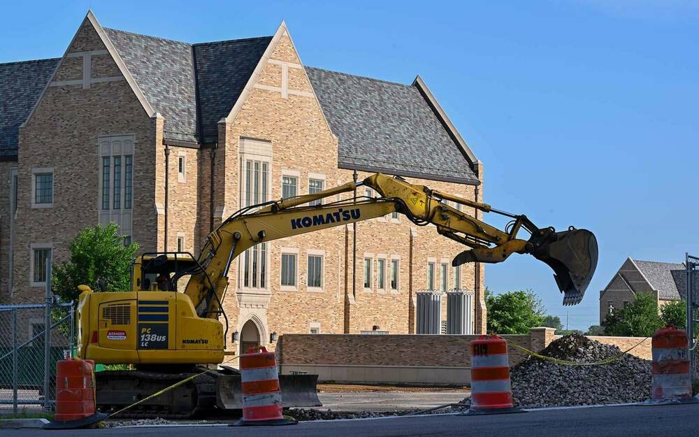 Construction work being done in front of a building with a yellow excavator.