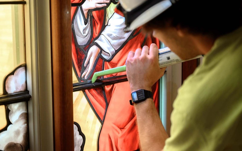 A man uses a caulk-like device to restore a stained glass window.